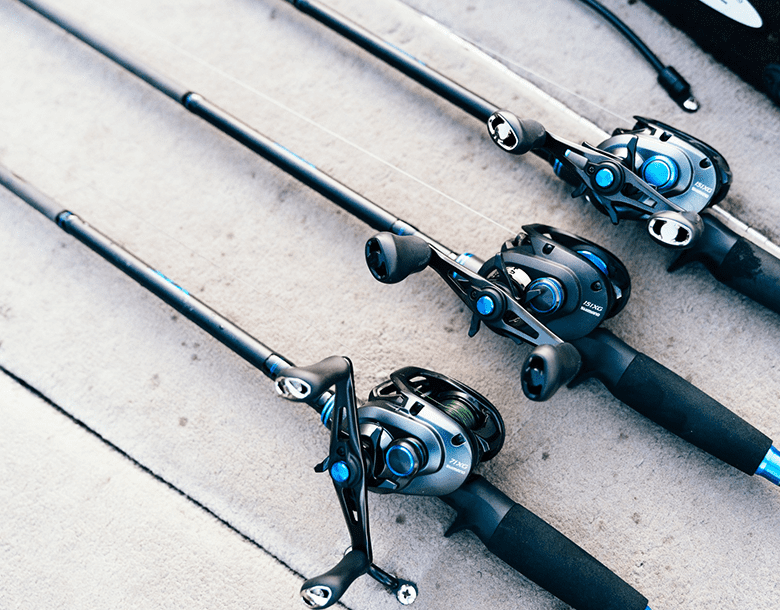 Three fishing rods and a reel on the ground.