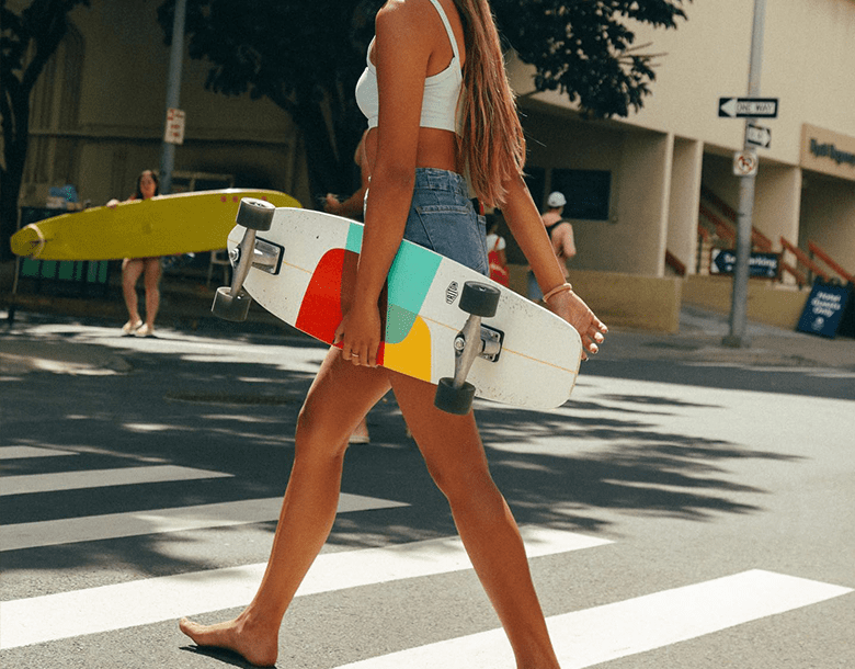 A woman walking down the street holding a skateboard.
