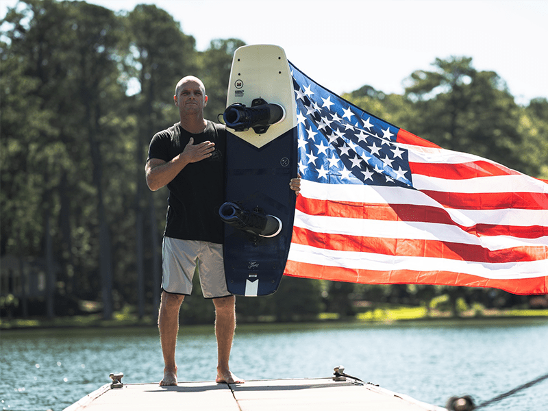 A man holding onto a kite board in front of an american flag.