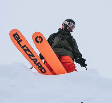 A person in orange jacket holding ski 's on snow covered ground.